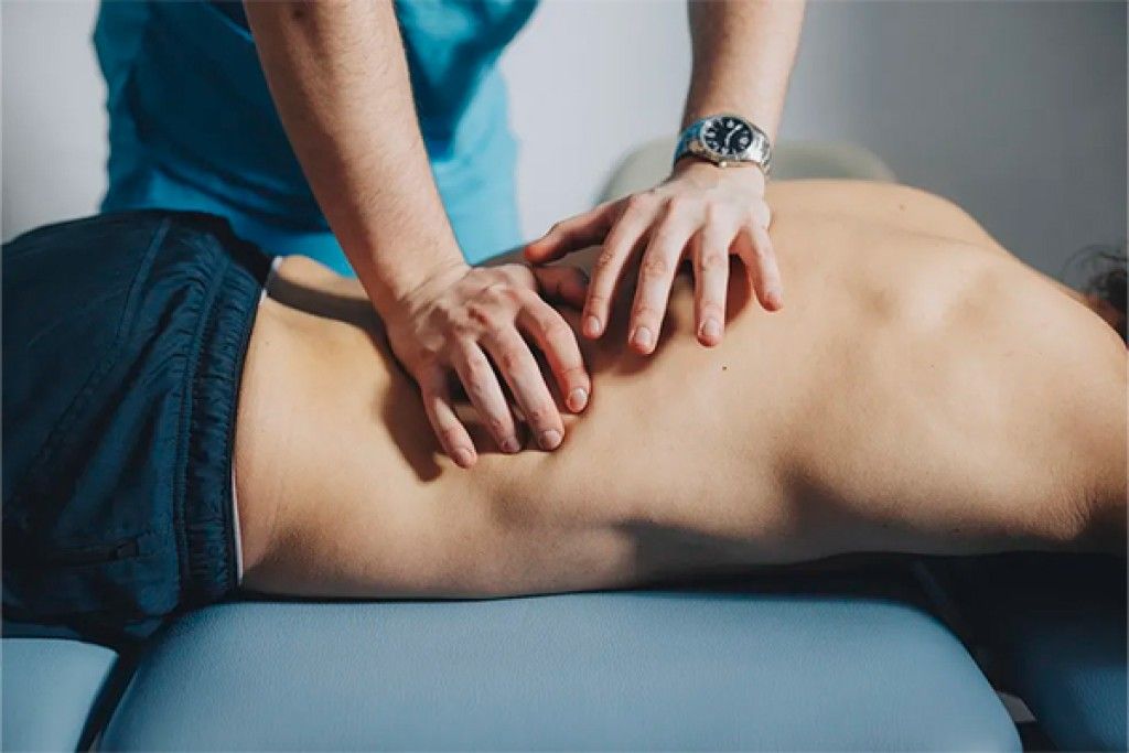 Manos de un terapeuta aplicando técnicas osteopáticas en la espalda de un paciente acostado en una camilla en Quironatura Torrox, ayudando a aliviar dolores y mejorar la movilidad.